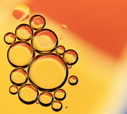Cluster of translucent oil bubbles on a gradient background transitioning from orange to yellow.