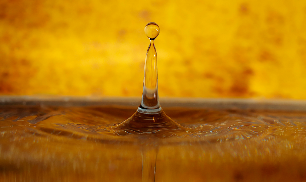 Close-up of a clear water droplet suspended above the surface against a golden-yellow blurred background.
