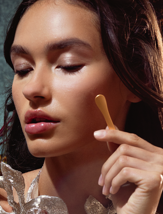 Close-up of a woman with closed eyes holding a small wooden spatula near her face.