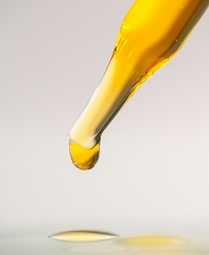 Close-up of a yellow liquid drop falling from a dropper against a soft beige background.