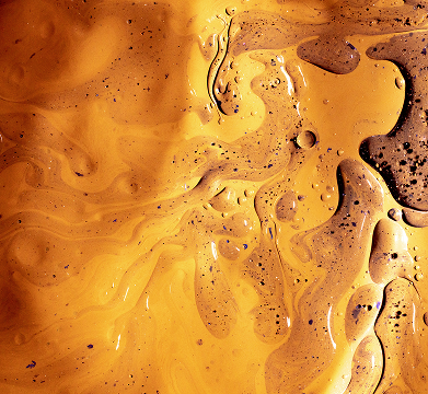Close-up of swirling golden-yellow and brown liquid with bubbles and speckles.