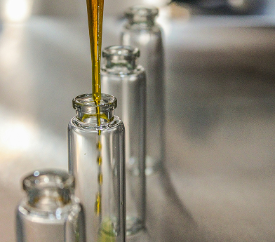 Golden liquid being poured into a small clear glass bottle, with two empty bottles blurred in the background.