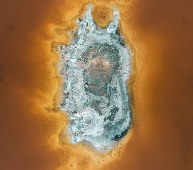 Aerial view of a salt formation with white and blue hues surrounded by orange-brown water.