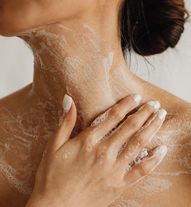 Close-up of a woman’s neck and chest with skincare cream applied while her hand gently touches her neck.
