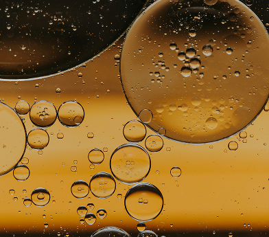 Close-up of translucent oil bubbles suspended in water with a warm yellow background.