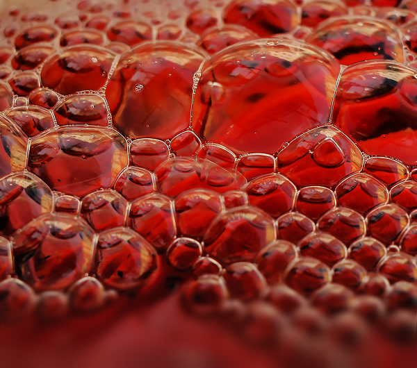 Close-up of translucent bubbles clustered together on a red liquid surface.