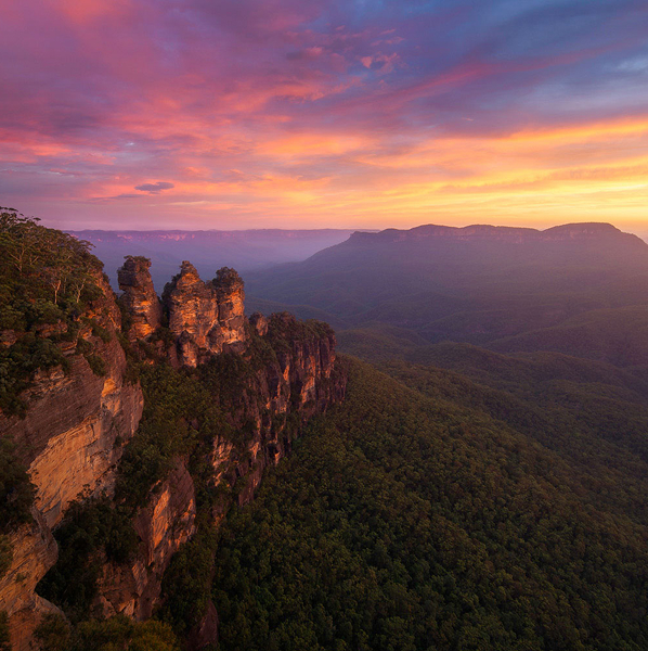 Sunset over the Three Sisters rock formation and forested valley in Blue Mountains, Australia.