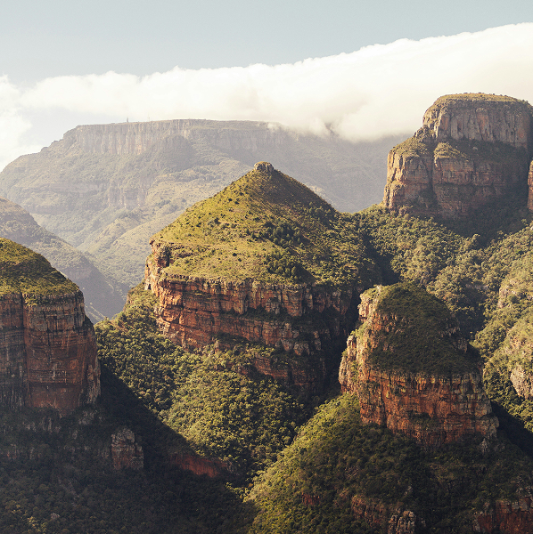Rock formations covered with green vegetation under a cloudy sky in a mountainous landscape.