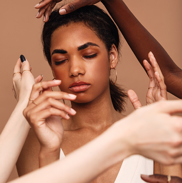 Woman with closed eyes surrounded by diverse hands in front of a beige background.