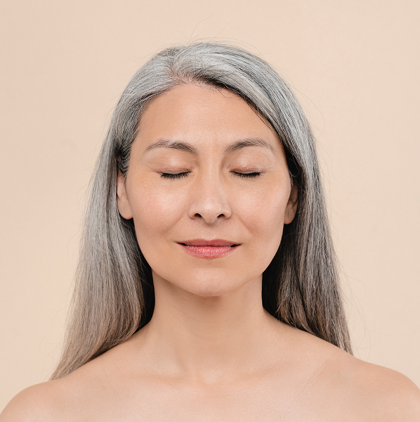 Middle-aged woman with long gray hair and closed eyes smiling softly against a beige background.