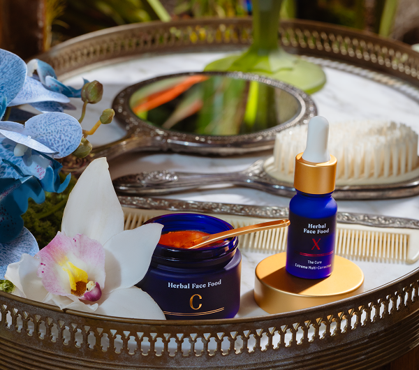 Tray with herbal face food jars labeled C and X, a floral orchid, a comb, a brush, ornate hand mirrors, and greenery in the background.