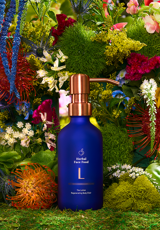 Blue Herbal Face Food lotion bottle with copper pump surrounded by colorful flowers and green foliage.