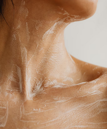Close-up of a person's neck and shoulder with white cream applied on the skin.