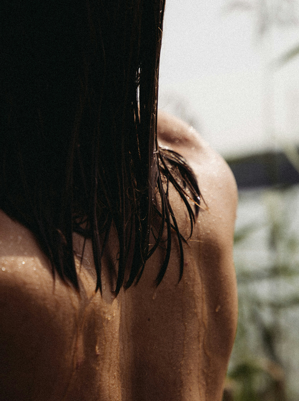 Close-up of a wet person’s back with water droplets and dark hair hanging down.