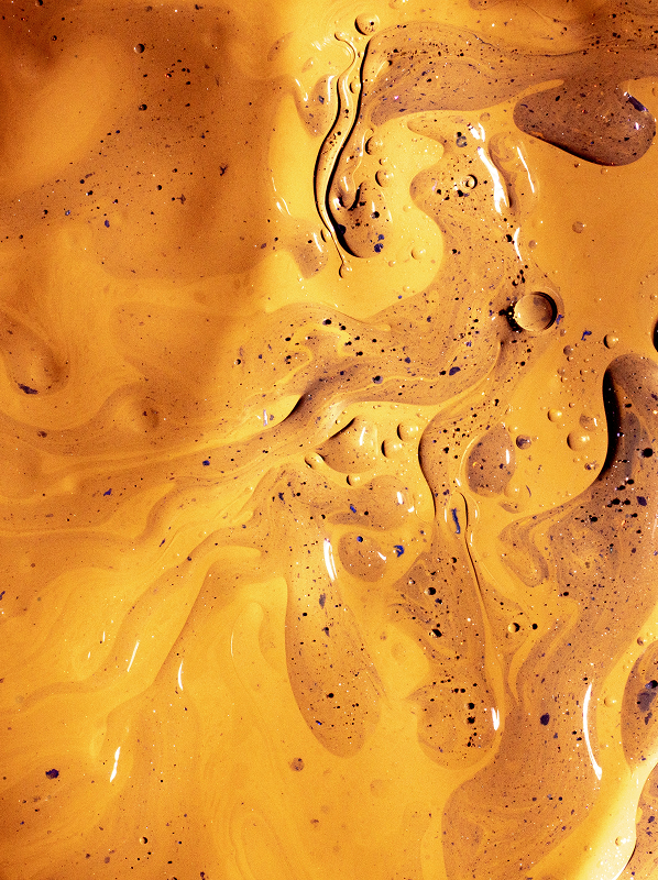 Close-up of swirling mustard yellow and brown liquid with bubbles and speckles creating an abstract pattern.