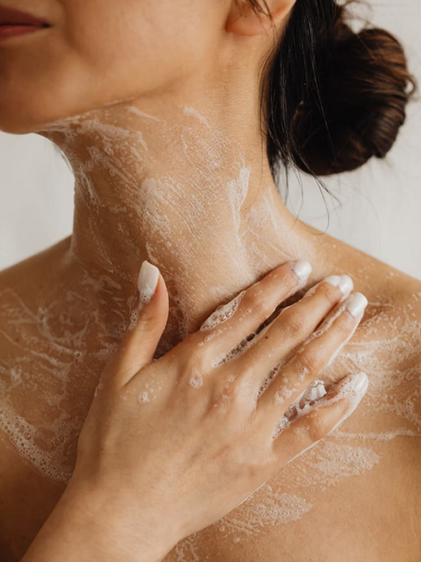 Close-up of a woman washing her neck and shoulder with soap suds, her hair tied back in a bun.