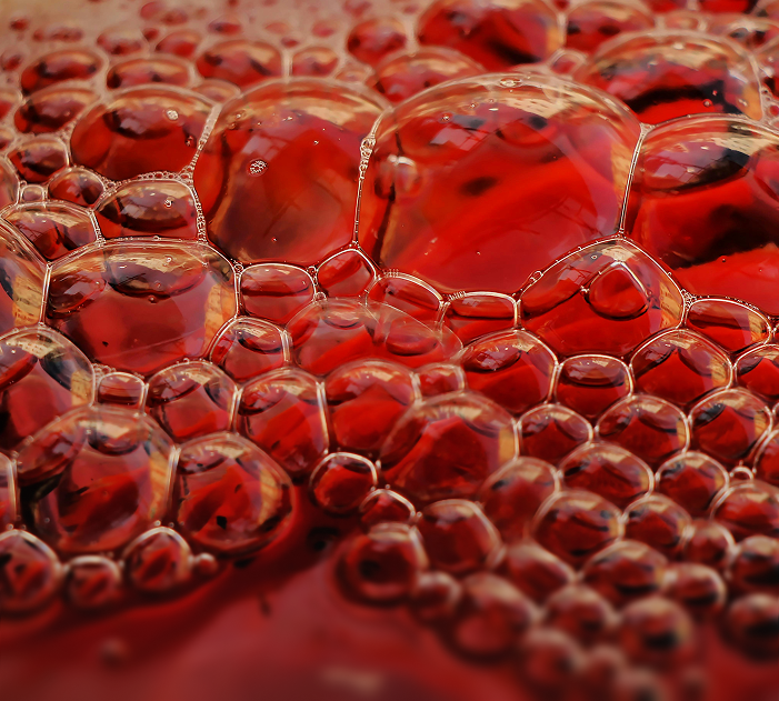 Close-up of numerous bubbles on the surface of a red liquid.
