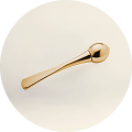 Gold-colored metal spoon with a rounded handle on a light surface.