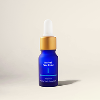 Blue glass bottle of herbal face food serum with a white dropper and gold collar on a beige background.