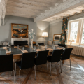 Bright meeting room with a large wooden table, ten black chairs, a lamp, a large window, and an abstract painting on the wall.