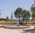 Round fountain in the center of a dry courtyard with trees and sea views in the background.