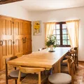 Dining room with large wooden table, chairs, chairs, plants and natural light through the window.
