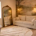 Living room with beige sofa, large mirror, thick carpet and wall decorated with plants and soft lighting.