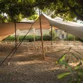 Traditional beige berber tent with wooden posts and landscape with trees in the background.