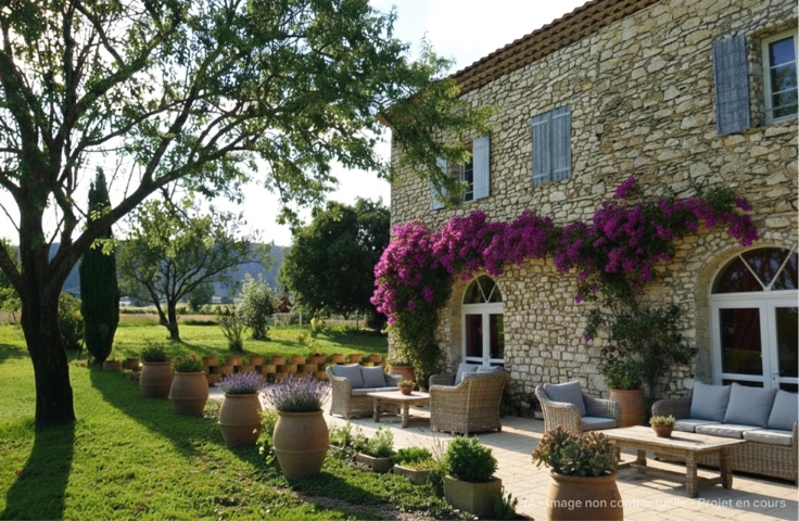 Terrasse provençale et façade de mas en pierre, salons de jardin en rotin avec coussins gris, grands pots en terre cuite remplis de lavande, olivier à gauche, pelouse et paysage de campagne