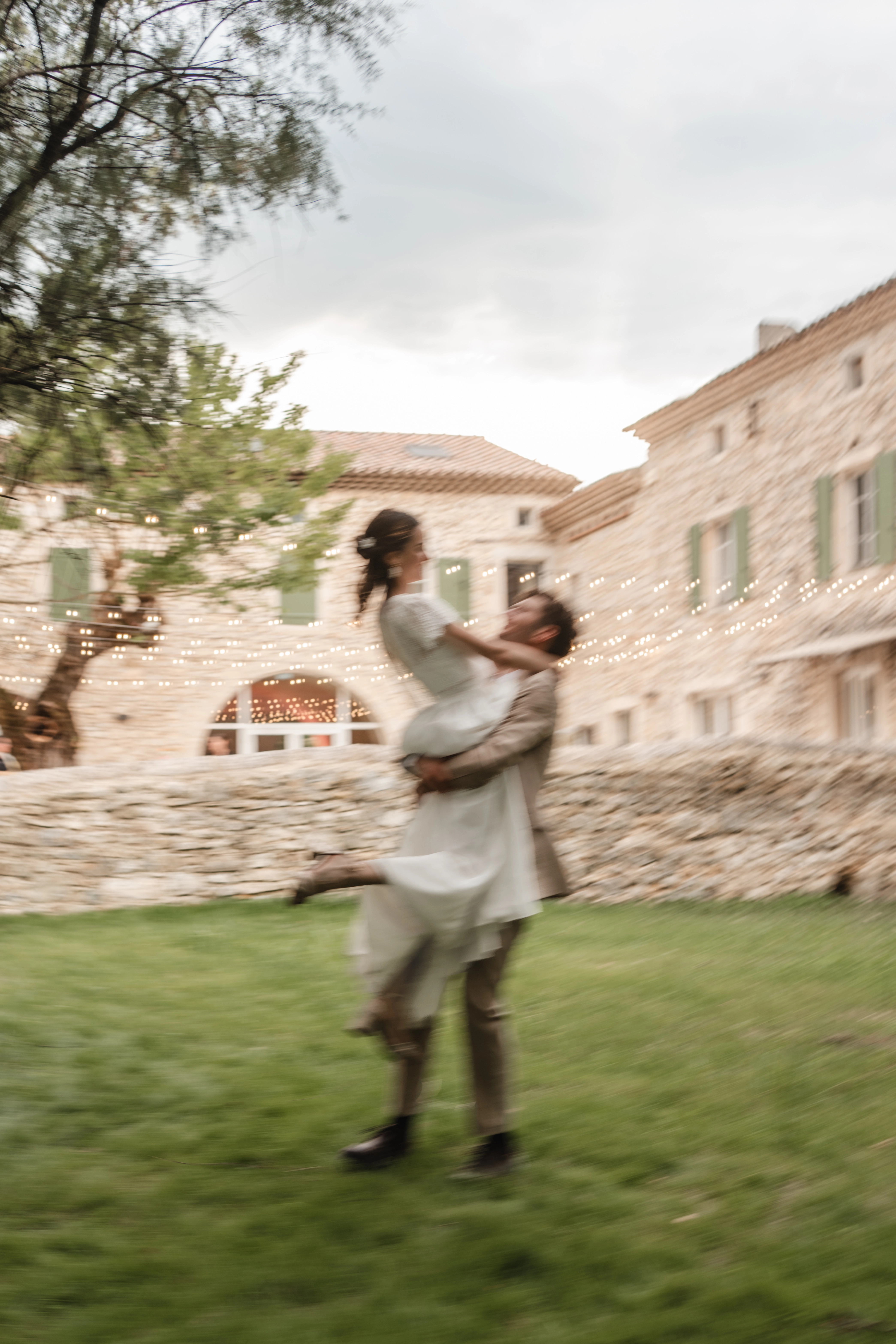 Portrait de mariage au Domaine de la Vivande, couple de mariés assis sur un banc en pierre, mariée en robe de mariée blanche, marié en costume beige, jardin provençal,