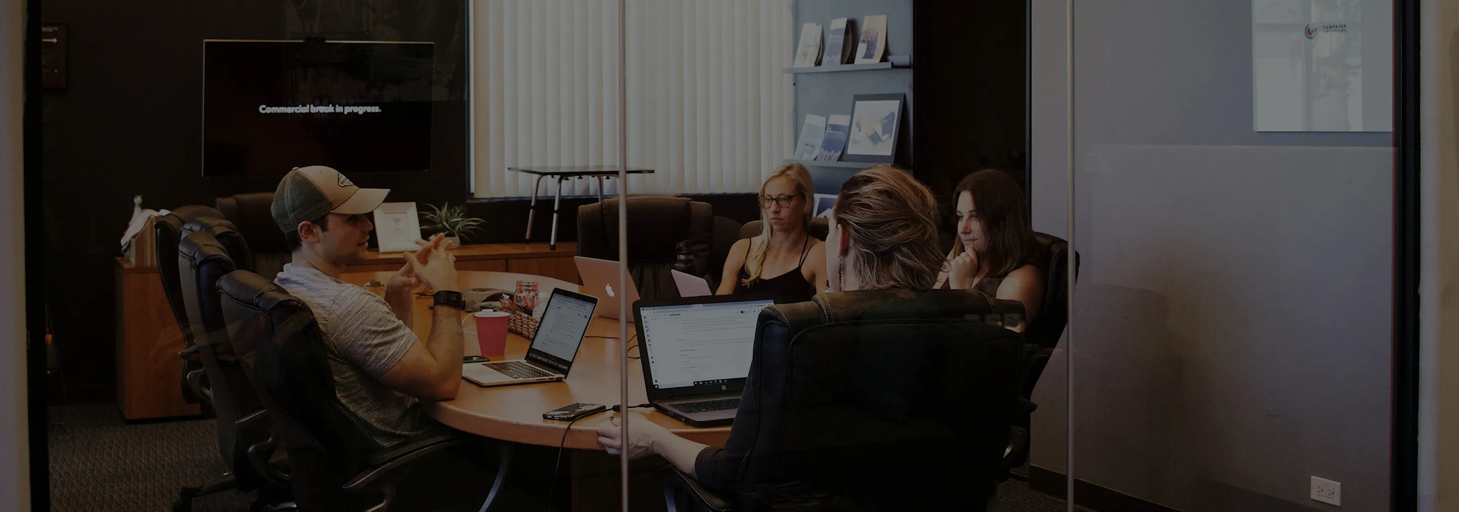 Four people sitting around a conference table in an office, working on laptops and engaged in discussion.