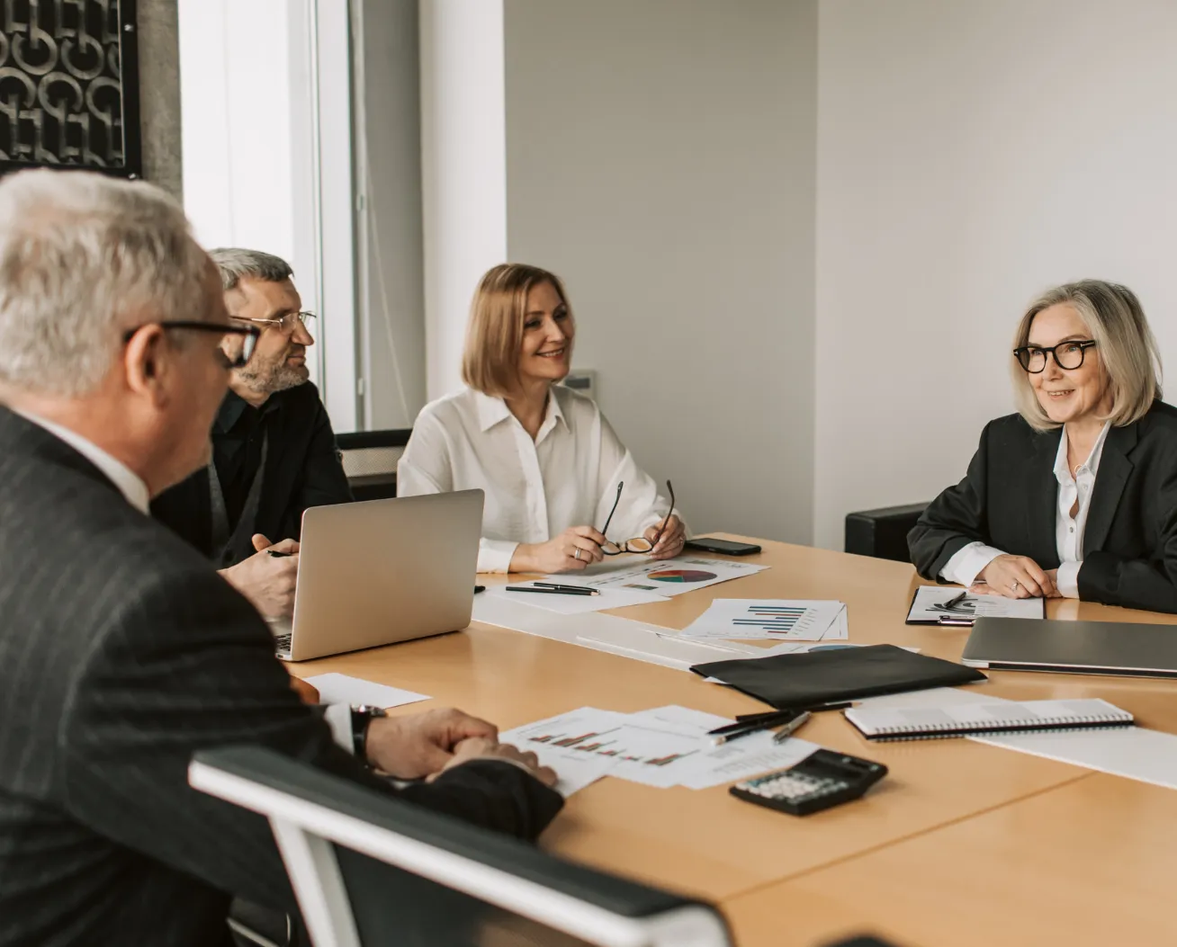 Four business professionals having a meeting around a table with laptops, documents, and a calculator.