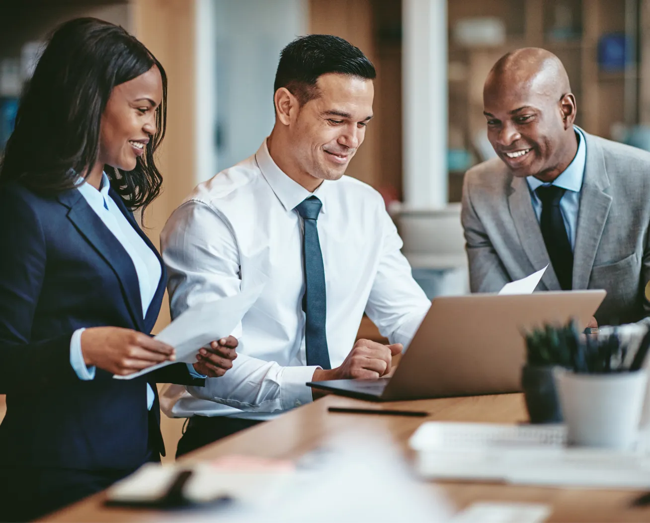 Three business professionals reviewing documents and working together on a laptop in an office.