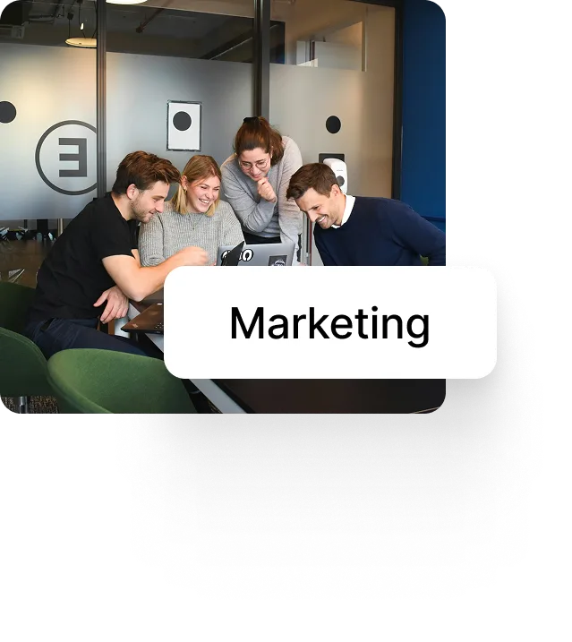 Four young professionals collaborating and smiling around a laptop in a modern office meeting room.