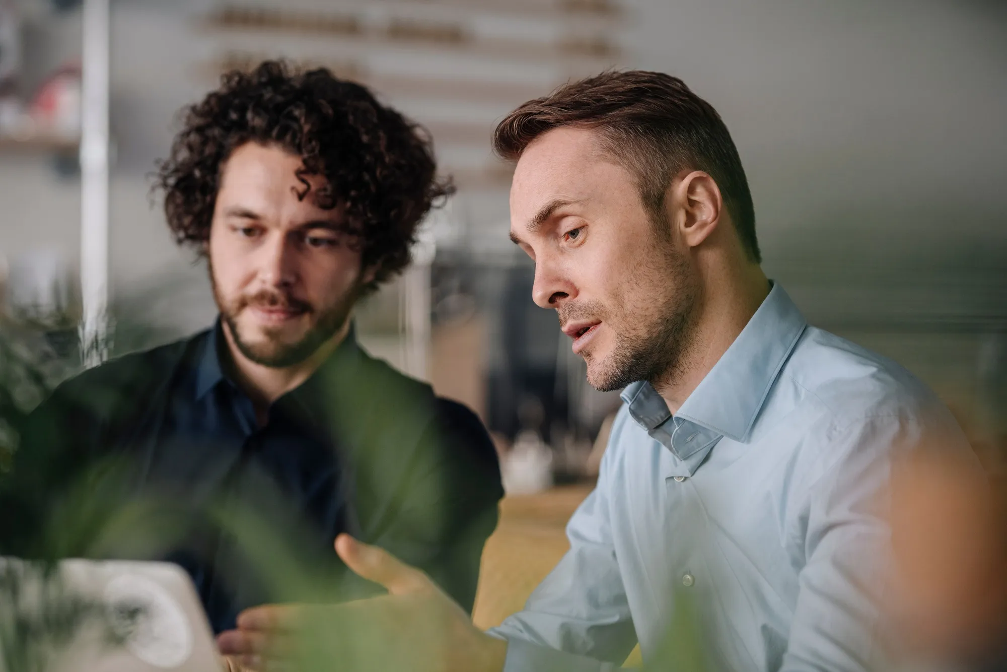 Two businessmen in suits having a discussion with coffee cups, laptop, and documents on the table.