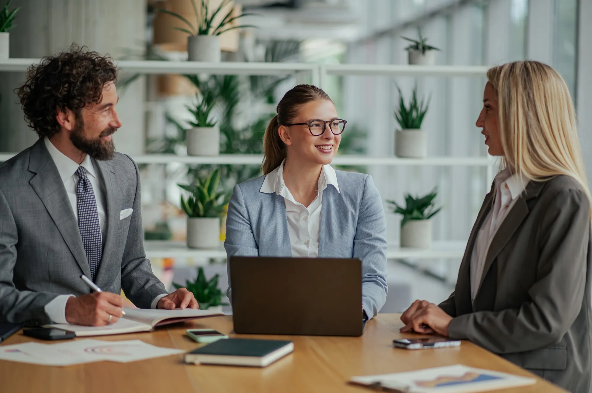 Young woman in white blouse sitting at desk using a computer mouse, with keyboard and notebook in a modern office.