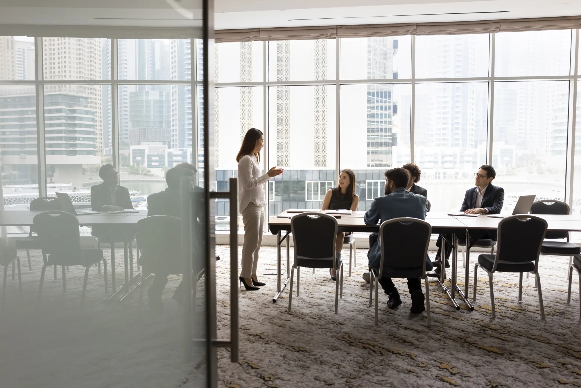 Two business professionals shaking hands while two colleagues smile and converse in a modern office setting.