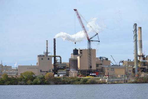 Industrial facility with smokestacks and a crane beside a body of water