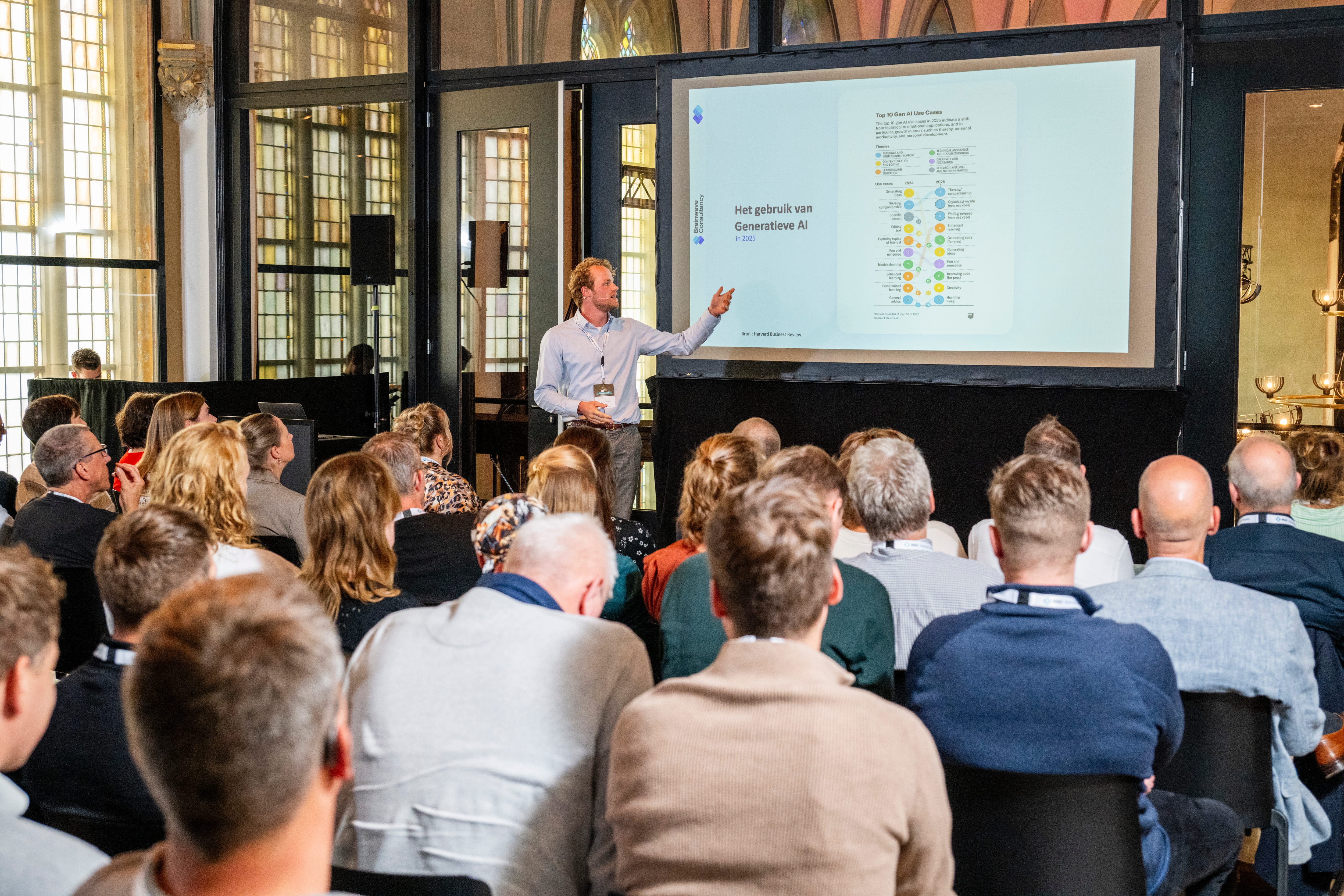 Speaker in a light blue shirt presenting a slide about Generative AI to an audience in a well-lit historic room.