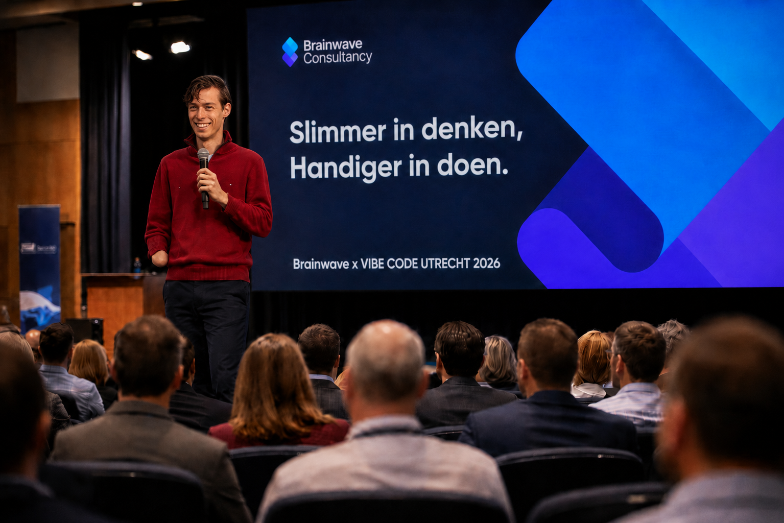 Speaker talking about 'vibe coding' Claude Code and ChatGPT  holding a microphone in front of an audience displaying Brainwave Consultancy branding and the text 'Slimmer in denken, Handiger in doen.'