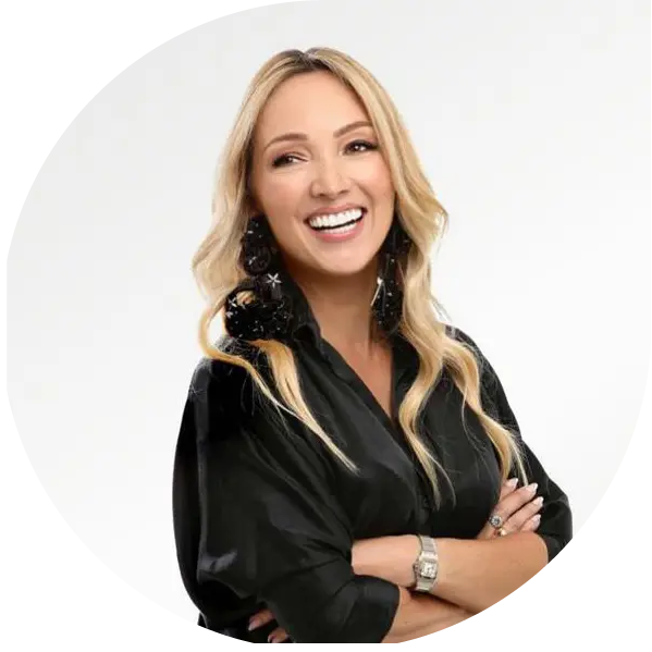 Smiling blonde woman with long hair wearing a black blouse and large earrings, arms crossed.