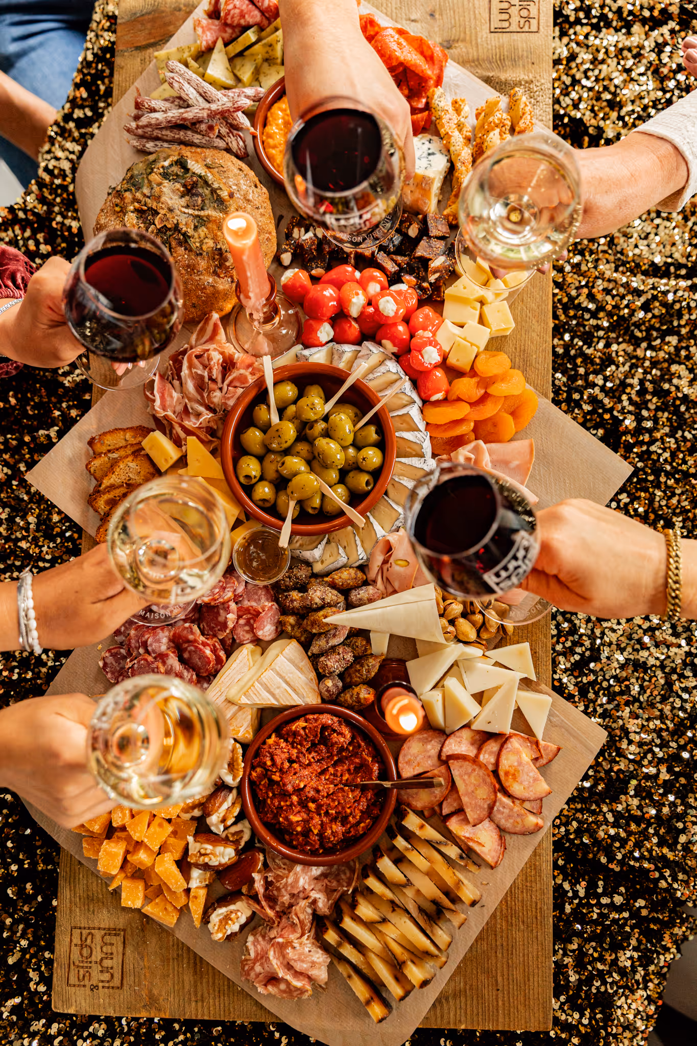 A picture of people sitting around a charcuterie board saluting with glasses of wine