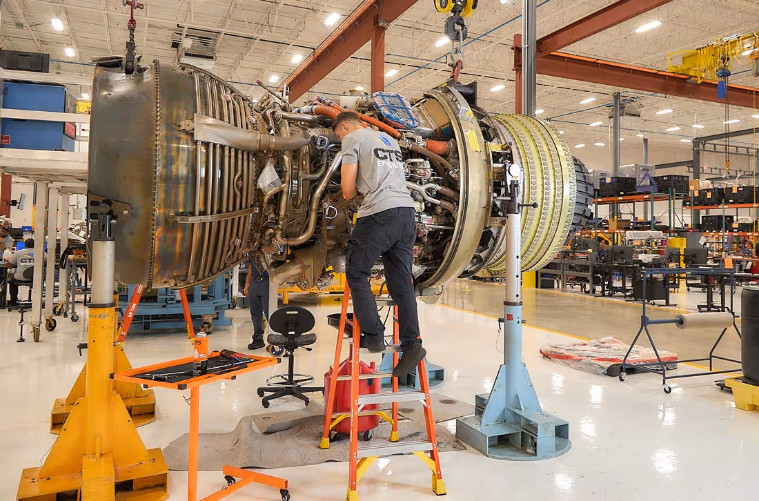 Technician working on a large jet engine suspended in CTS Engines Shop