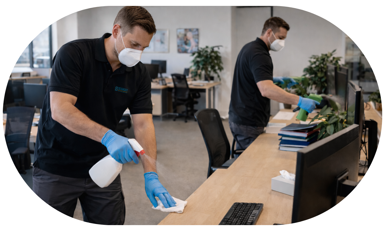 Man wearing a mask and gloves disinfecting an office desk with a spray bottle and cloth.