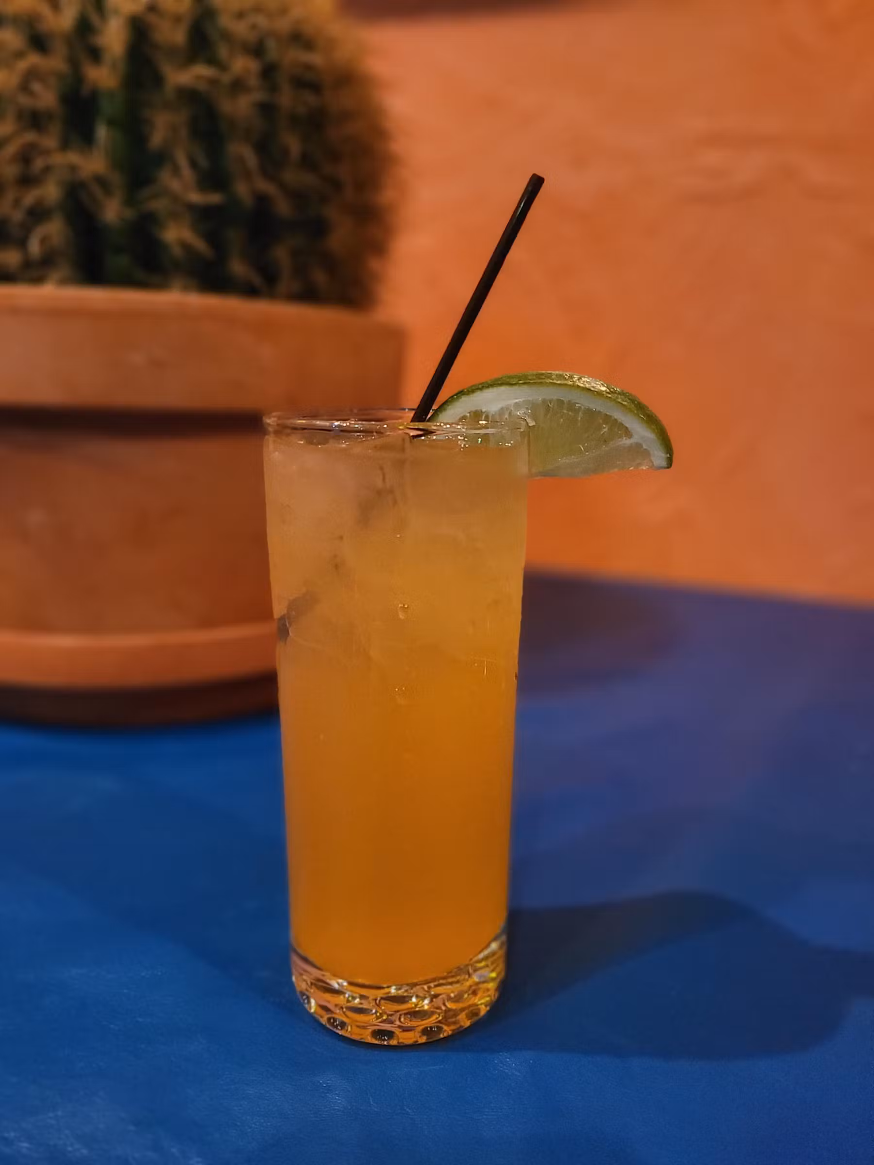 An orange beverage garnished with lime served in a blue table.
