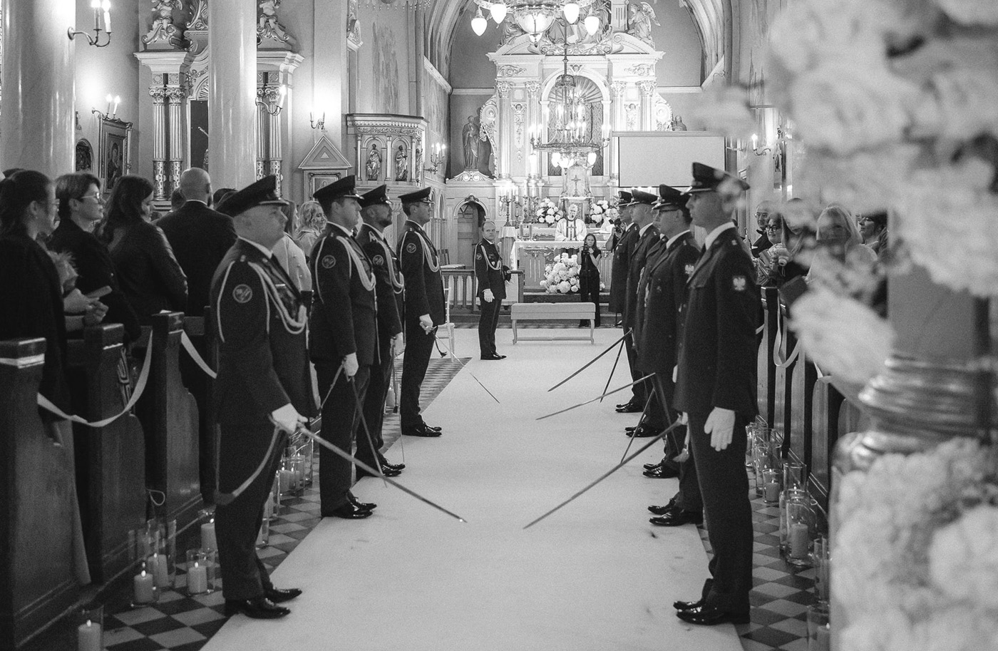 Uniformed men holding swords forming an archway in a decorated church with guests seated on either side.