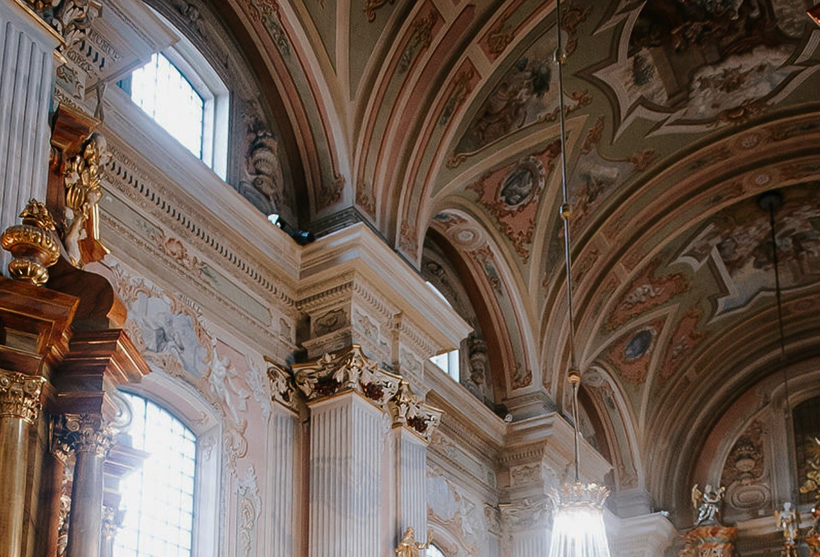 Ornate baroque church interior with decorated arches, gold accents, and tall windows letting in light.
