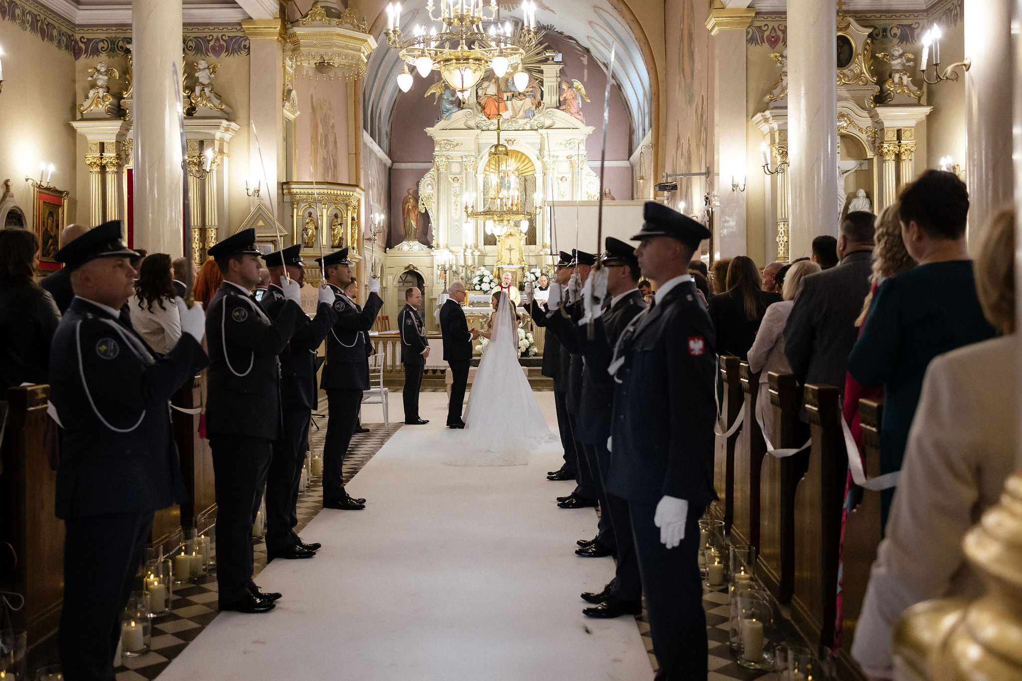 Bride and groom standing at the altar in a church with uniformed guards holding swords forming an arch along the aisle.