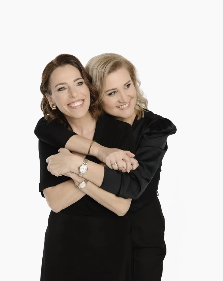 Woman in white suit standing beside a pyramid of champagne glasses on an illuminated round platform in a dimly lit, elegant venue with golden curtains and candles in the background.