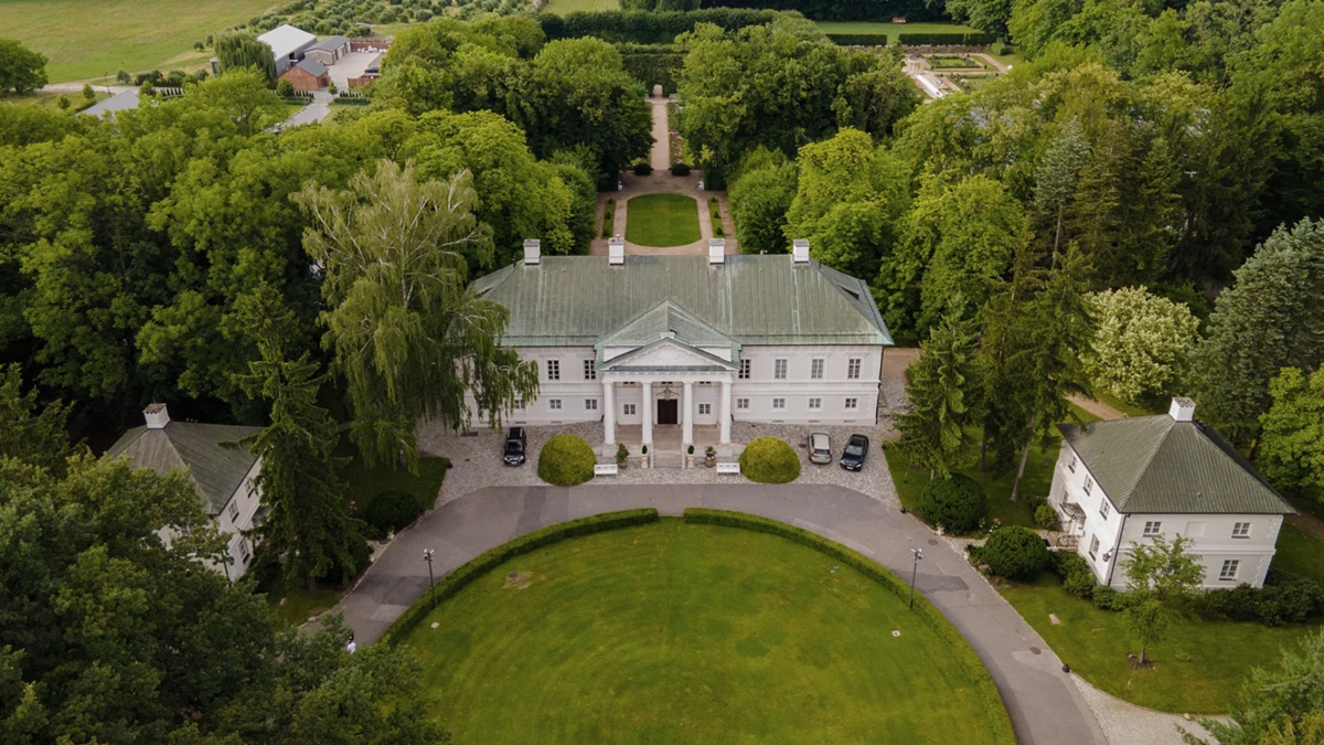 Symmetrical white neoclassical building facade with multiple windows, central portico entrance, and two street lamps on a clear day.